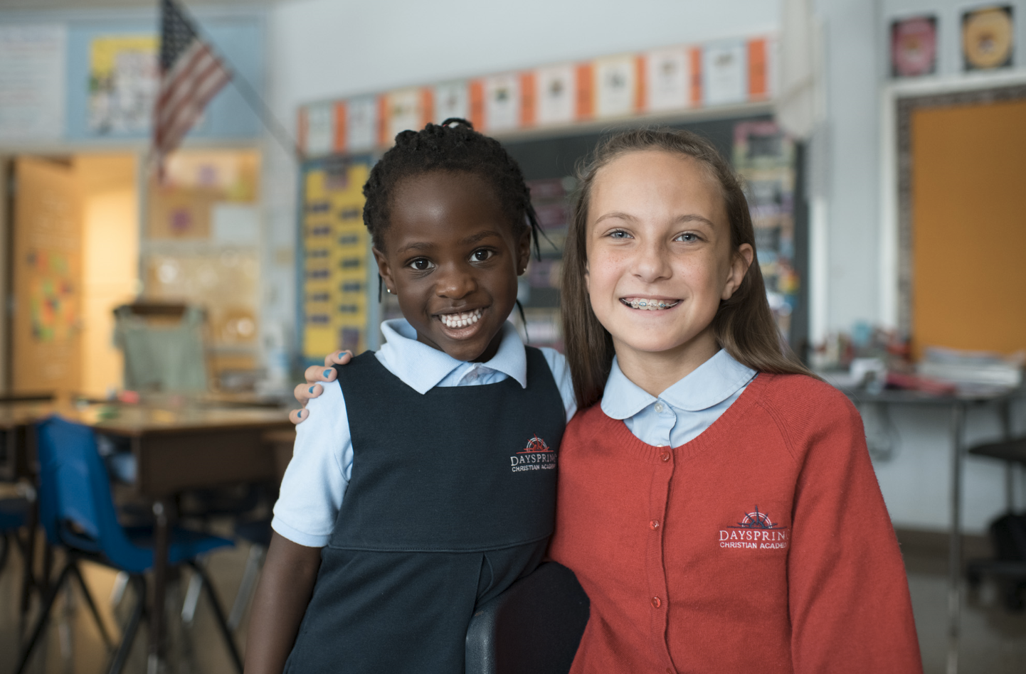 Two smiling female students sit in a classroom at Dayspring Christian Academy.